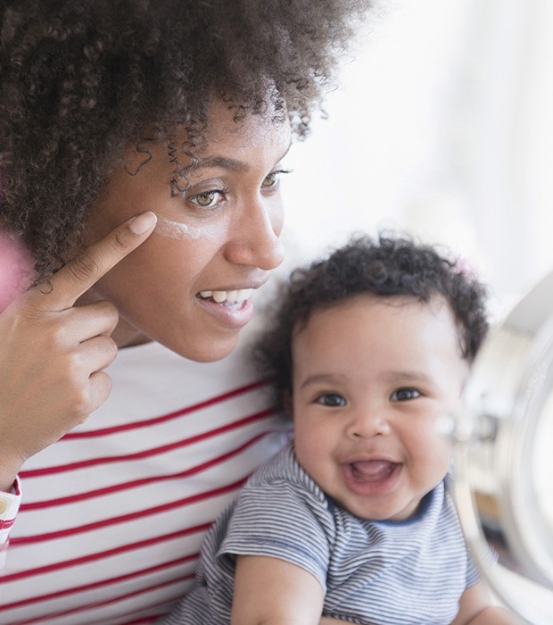 Mother holding baby son applying face cream in mirror (Foto: Getty Images/Blend Images)