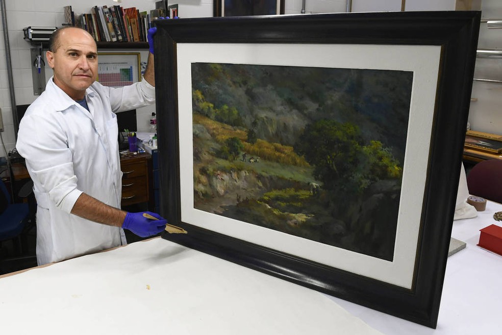 O restaurador Nonato Nascimento mostra a obra "Trigal na serra", de Guido Mondin: tela recuperada após atos golpistas — Foto: Jefferson Rudy/Agência Senado