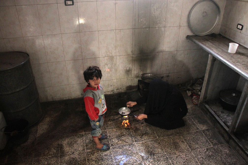 Mulher cozinha pó a base de arroz na cozinha de sua casa em Duma, na Síria (Foto: Hamza Al-Ajweh/AFP)