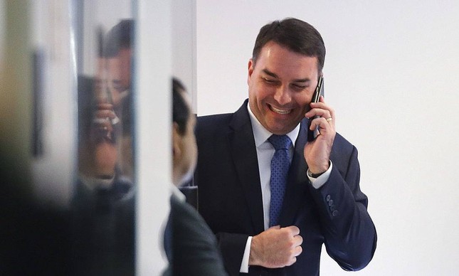 O senador Flávio Bolsonaro sorri enquanto fala no celular