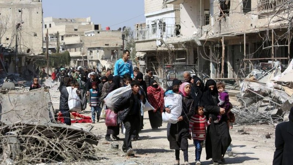 Civis deixam a cidade de Jisreen, com prédios destruídos pela guerra, em 2017 — Foto: Getty Images/AFP/BBC