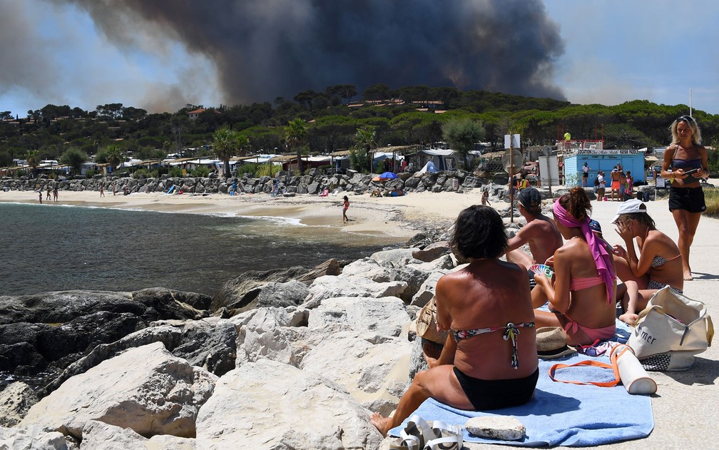 Banhistas jogam cartas na praia enquanto observam incêndio florestal em Bormes-les-Mimosas, na França, na quarta-feira (26) (Foto: Anne-Christine Poujoulat/AFP)