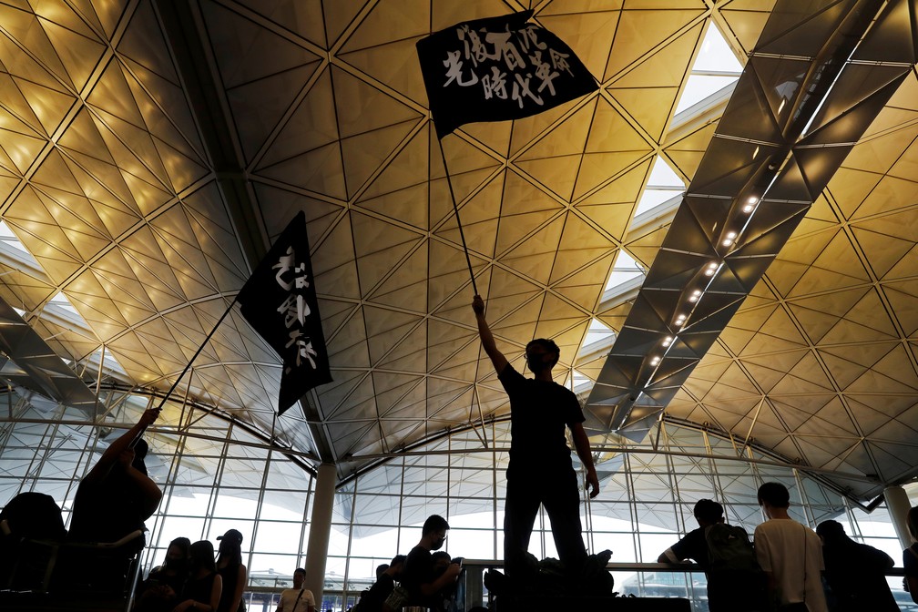 Manifestante segura uma bandeira com caracteres chineses que dizem "LIbertem Hong Kong, a revolução de nossos tempos" em uma manifestação no aeroporto da cidade nesta segunda-feira (12).  — Foto: Tyrone Siu/Reuters