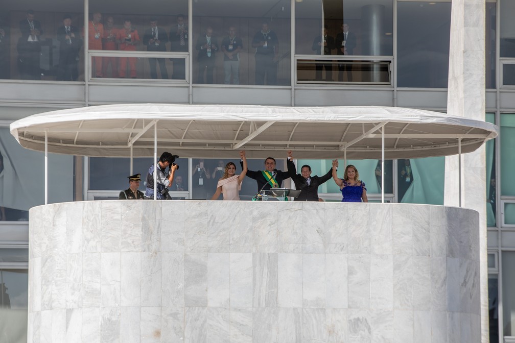Jair Bolsonaro e Hamilton Mourão erguem os braços com suas mulheres no Parlatório, diante do público que assiste  a cerimônia — Foto: Fábio Tito/G1