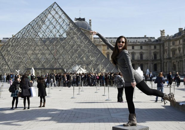 Turista posa para foto em frente à pirâmide do Museu do Louvre, em Paris (Foto: Loic Venance/AFP)