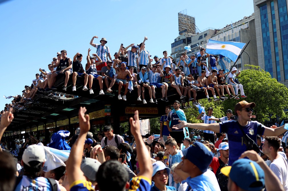Torcedores se aglomeram em cima de uma marquise para ver o ônibus com a seleção campeã da Copa do Mundo de 2022, em Buenos Aires, na Argentina, em 20 de dezembro de 2022.  — Foto: Cristina Sille/ Reuters