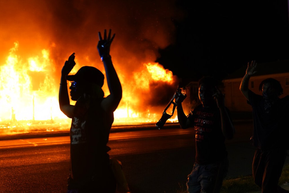 Manifestantes passam com mãos ao alto diante de policiais em Kenosha, no Wisconsin (EUA), após novos protestos contra o racismo e a violência policial terminarem em confronto na noite de segunda-feira (24) — Foto: David Goldman/AP