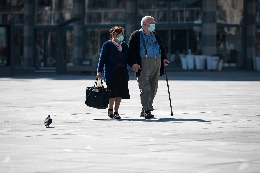 Um casal de idosos usando máscaras de proteção caminha pela praça principal de Belgrado, na Sérvia — Foto: Andrej Isakovic/AFP
