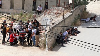 Palestinos se protegem durante confrontos com forças de segurança israelenses na cidade de Jenin, na Cisjordânia. Um palestino foi ferido por fogo israelense durante uma operação na cidade ocupada de JeninAFP
