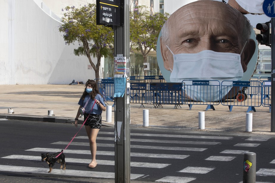 Mulher caminha com cachorro perto de cartaz encoraja população a usar a máscara contra covid-19 em Tel Aviv, Israel
