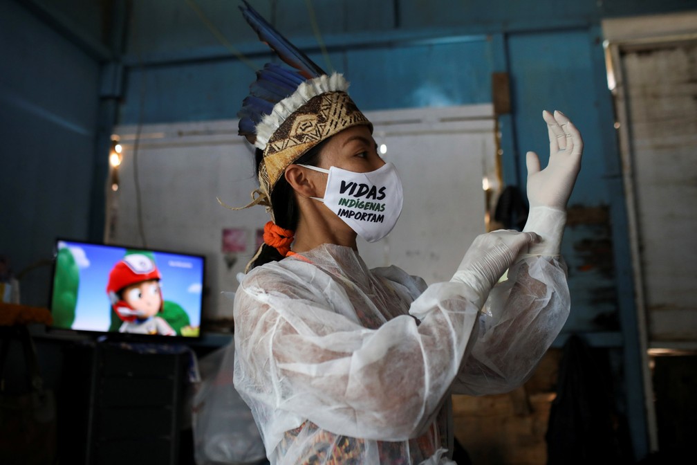 Vanda usa uma máscara com a mensagem 'Vidas indígenas importam' enquanto coloca equipamentos de proteção individual antes de sair de casa — Foto: Bruno Kelly/Reuters