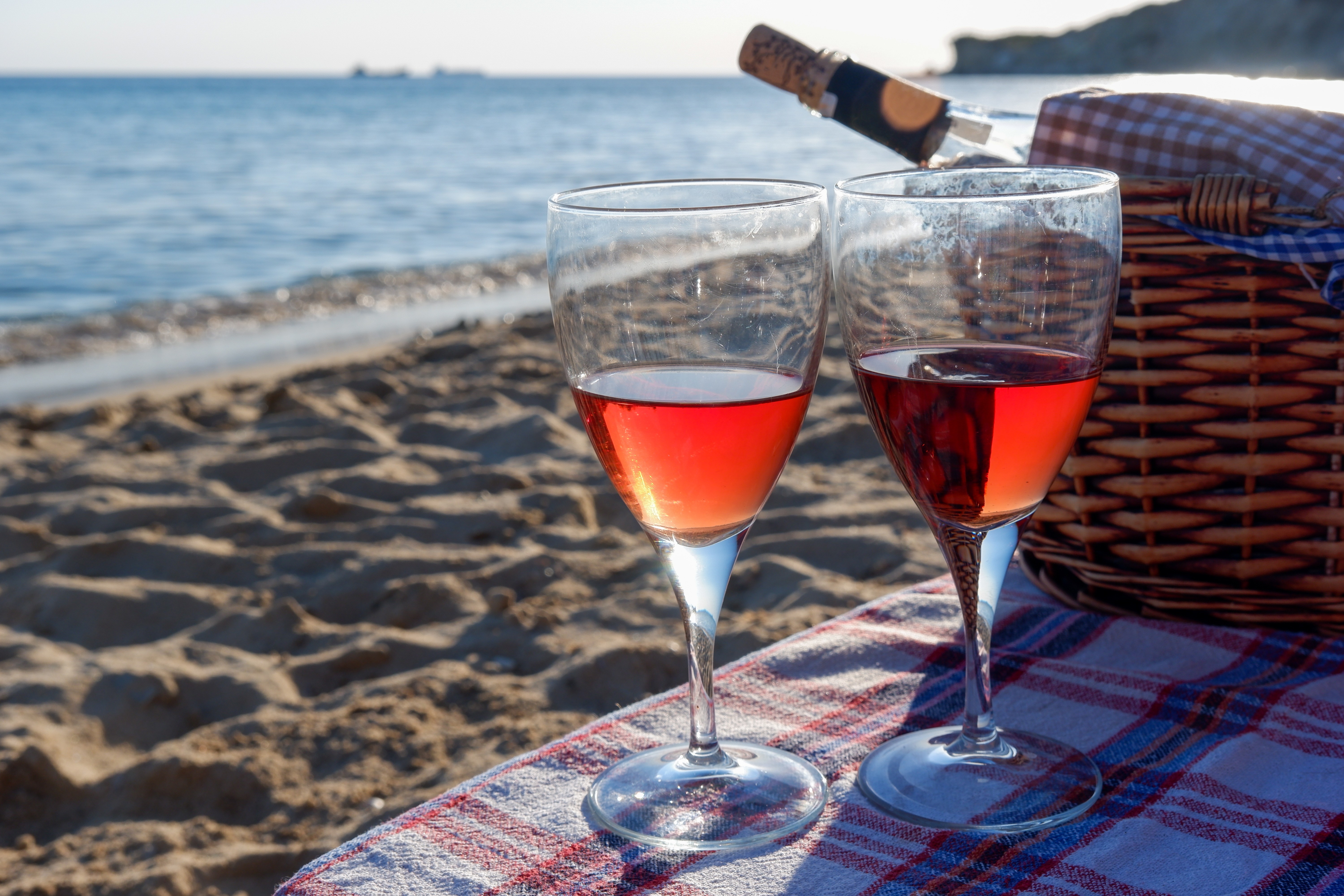 A bottle of rose wine in a wicker picnic basket and two glasses of rose wine next to it on a plaid tablecloth. Focus on foreground. A romantic summer vacation concept. (Foto: Getty Images/iStockphoto)