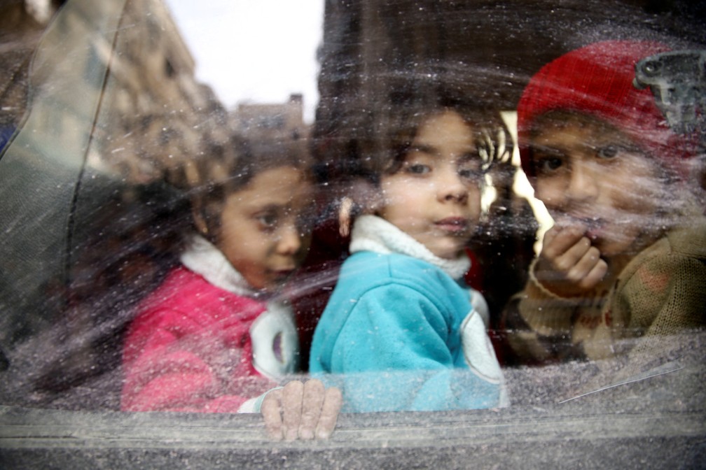 CrianÃ§as olham pela janela de um Ã´nibus durante uma evacuaÃ§Ã£o da cidade de Douma, na SÃ­ria (Foto: Bassam Khabieh/Reuters)
