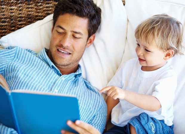 Pai e filho lendo livro juntos no sofá (Foto: Shutterstock)