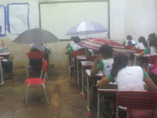 Após chuva, sala de aula das escola municipal Guilherme Dourado ficou alagada e alunos tiveram que se proteger com guarda-chuvas (Foto: Uiliene Santa Rosa)