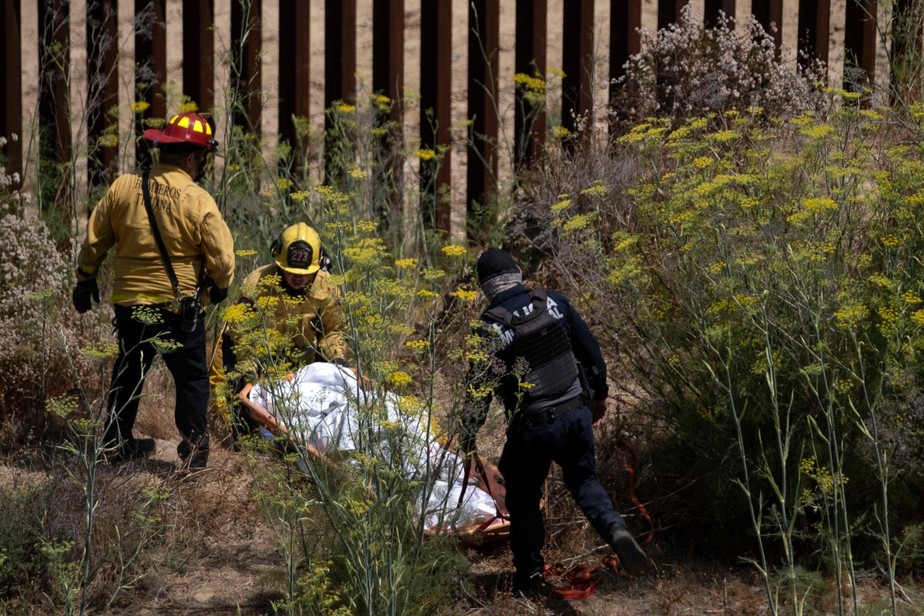 Bombeiros carregam o corpo de suposto coiote morto na fronteira do México com os EUA, em Tijuana, no estado mexicano da Baja Califórnia