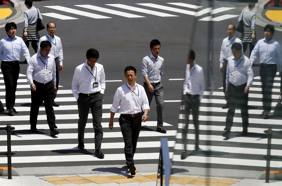 Imagens de trabalhadores refletidas em vidro enquanto atravessam a rua durante a hora do almoço em Tóquio (Foto: Thomas Peter/Reuters)
