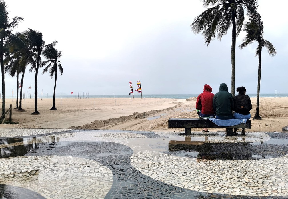 Pessoas se protegem do vento forte na orla da Zona Sul do Rio na manhã desta quinta-feira (11) — Foto: Marcos Serra Lima / g1