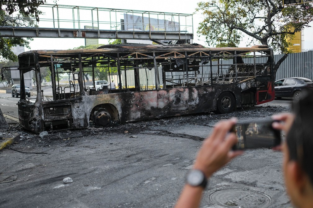 Homem fotografa nesta quarta-feira (1º) um ônibus queimado no dia anterior em Caracas — Foto: AFP/Matias Delacroix
