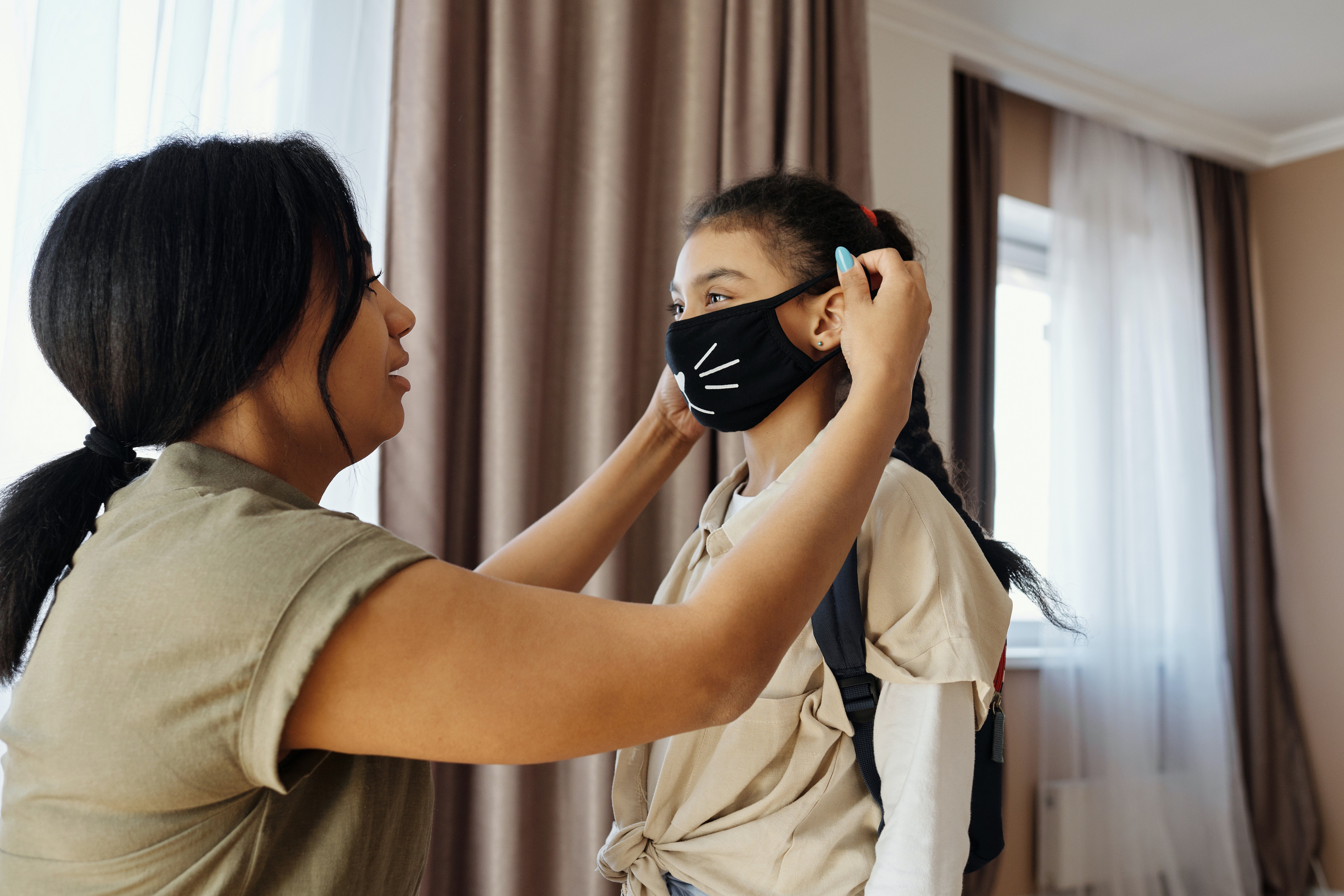 Mãe colocando máscara estampada na filha (Foto: Pexels)