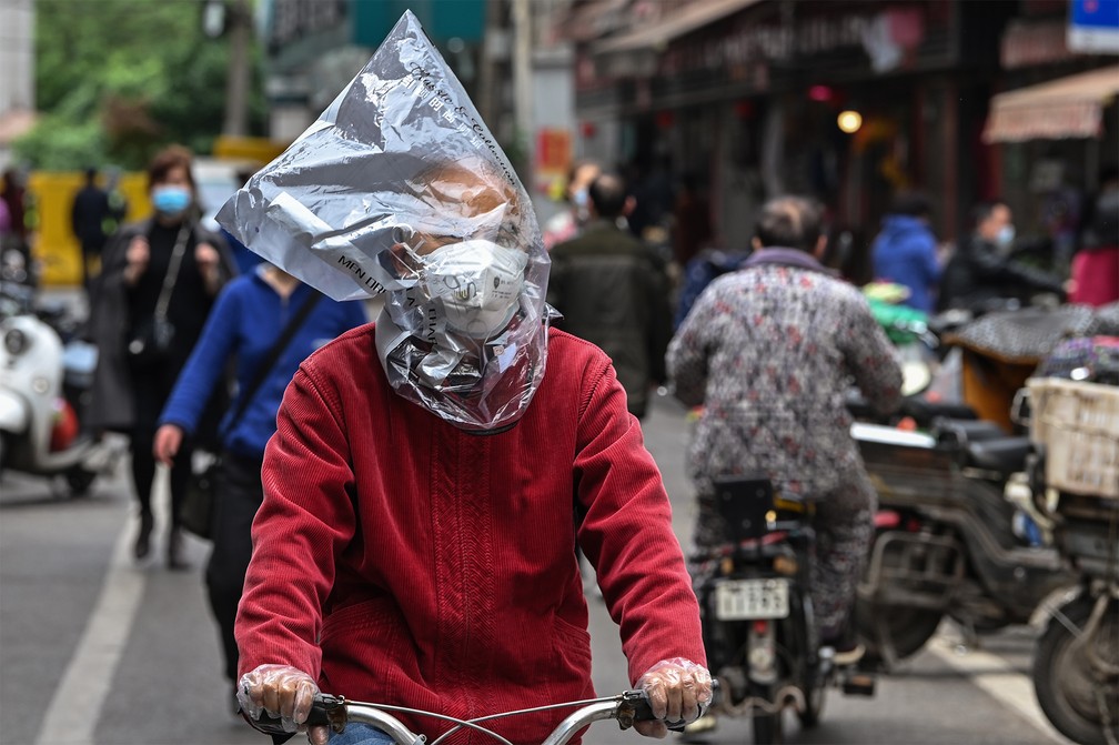 Com uma máscara e um saco plástico na cabeça, homem passa de bicicleta em uma rua de Wuhan, na China, onde teve início a epidemia de coronavírus — Foto: Hector Retamal/AFP