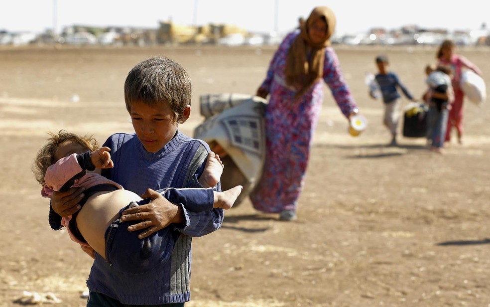 Jovem curdo sírio refugiado carrega uma criança após cruzar a fronteira entre a Síria e a Turquia, próximo a cidade turca de Suruç. Mais de 130 mil curdos sírios atravessaram a fronteira nos últimos 3 dias fugindo do avanço do grupo Estado Islâmico (Foto: Murad Sezer/Reuters)