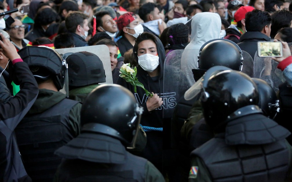 Manifestante segura flores enquanto encara policiais durante protesto em La Paz, na Bolívia, na terça-feira (22) — Foto: Reuters/David Mercado