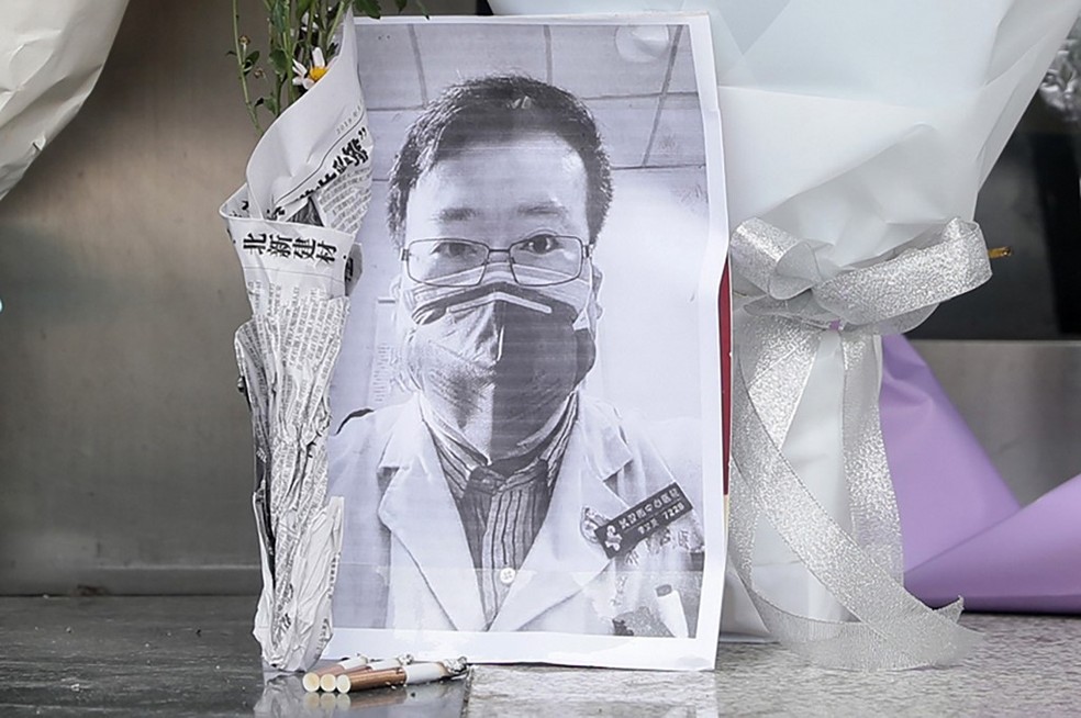 Imagem mostra foto do oftalmologista Li Wenliang, que morreu com coronavírus após ser reprimido pela polícia chinesa ao tentar alertar sobre o surto quando ele ainda estava no início. Retrato foi visto entre flores em frente ao Hospital Central de Wuhan, na China. — Foto: STR/ AFP