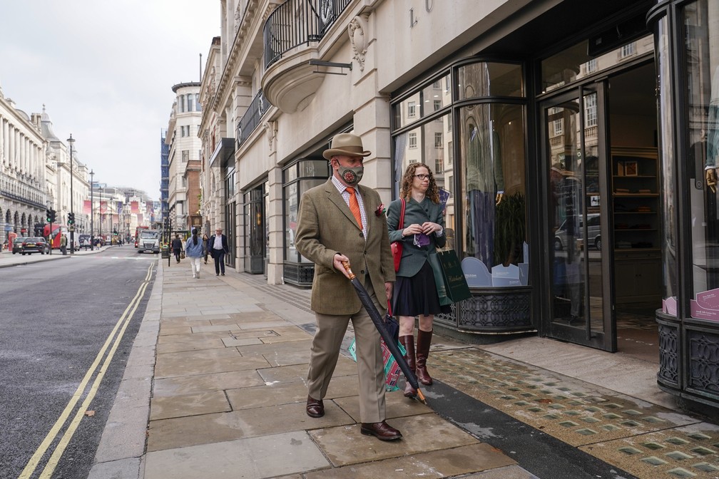 Homem usa máscara de proteção contra a Covid-19, mas mulher, não, enquanto os dois caminham por rua em Londres, na Inglaterra, em 19 de outubro de 2021 — Foto: Alberto Pezzali/AP