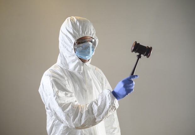  Homem com máscara, luvas e roupa de proteção, segurando um martelo de juízes (Foto:  Aitor Diago via Getty Images)