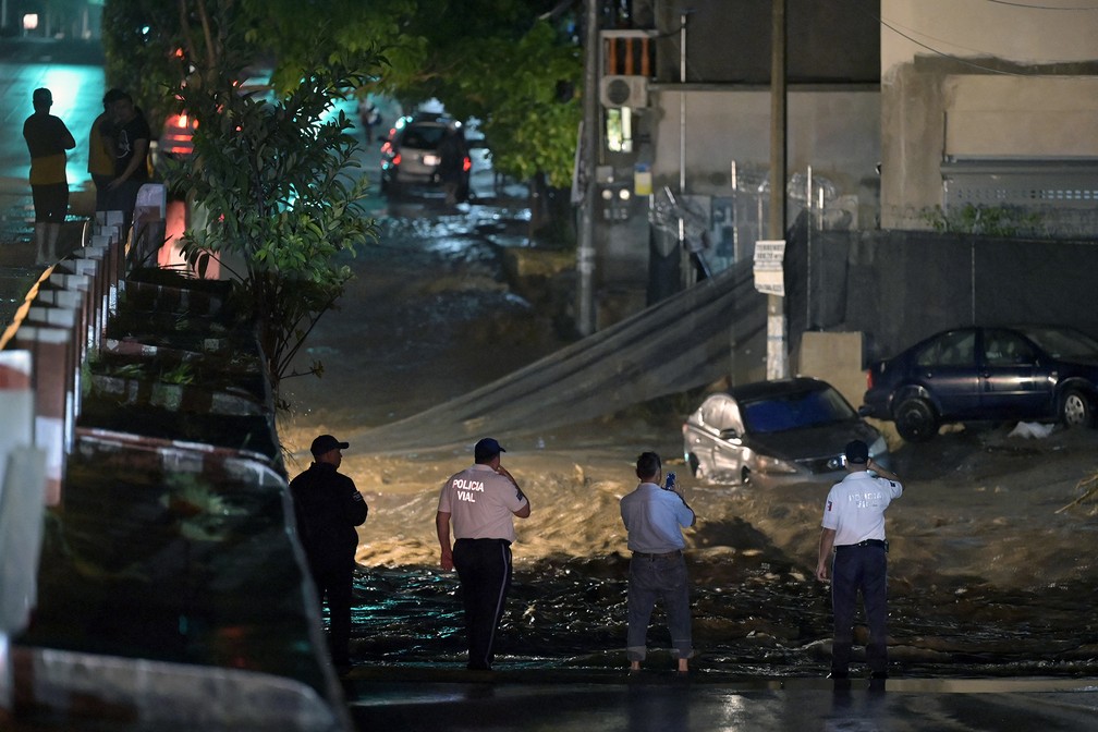 Policiais observam rua alagada após a chegada do furacão Roslyn em Puerto Vallarta, no estado de Jalisco, México, neste domingo. Posteriormente, o fenômeno perdeu força e foi rebaixado a tempestade tropical — Foto: Alfredo Estrella/AFP