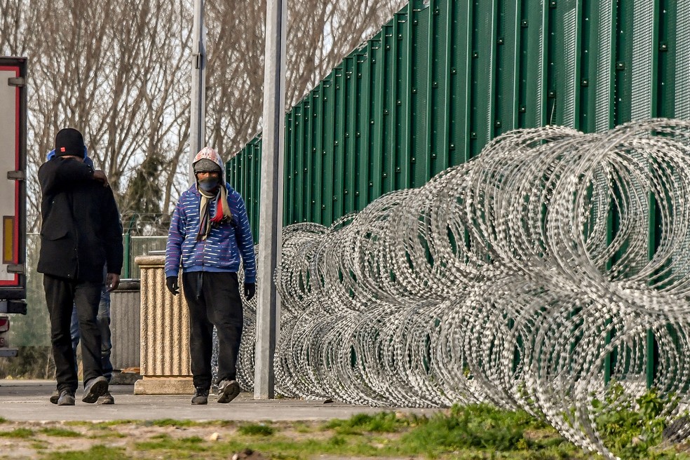 Grupo de migrantes caminha perto de estacionamento em Calais, na França (Foto: PHILIPPE HUGUEN / AFP)