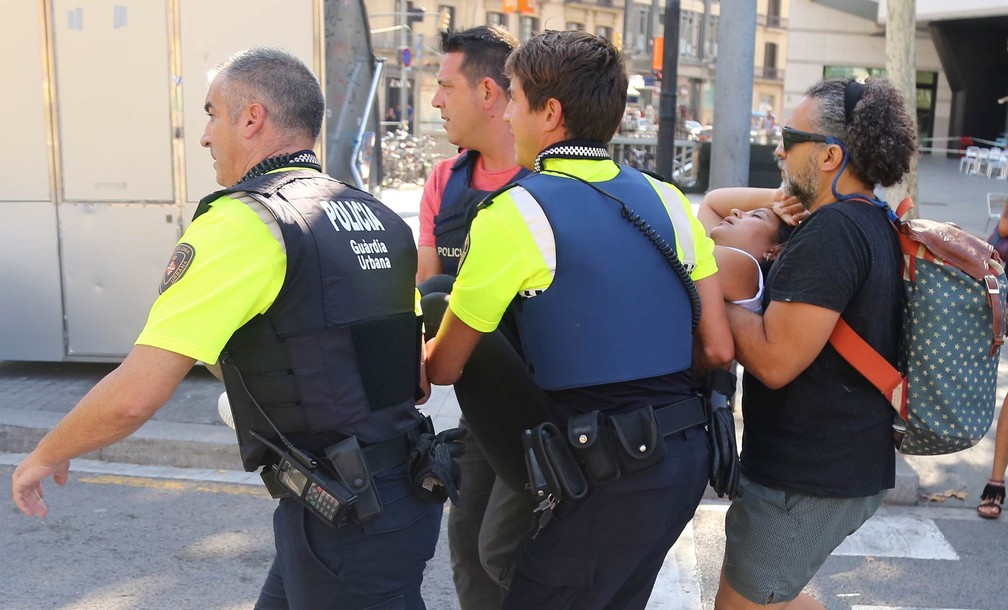 Mulher ferida é carregada por policiais e um homem após atentado com uma van usada para atropelar diversas pessoas na região de Las Ramblas, em Barcelona (Foto: Oriol Duran/AP)