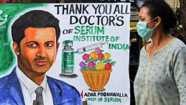 Uma mulher passa por uma pintura dando as boas-vindas ao programa de vacinação da Covid-19 com um retrato de Adar Poonawalla, CEO do Serum Institute of India (Foto: Foto de Ashish Vaishnav / SOPA Images / LightRocket via Getty Images)