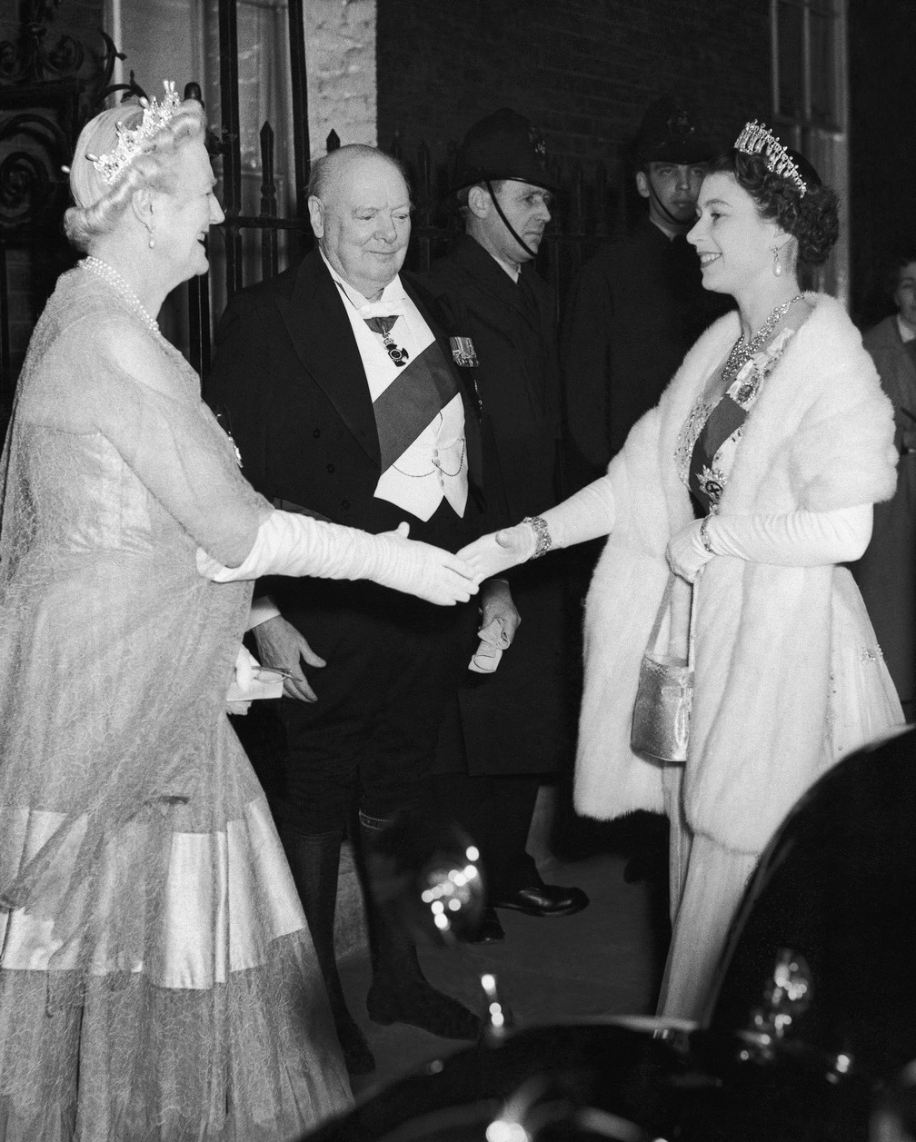 A Rainha Elizabeth II cumprimenta Clementine Churchill, esposa de Winston Churchill (ao fundo) em uma recepção para um jantar de gala em 1955. — Foto: ASSOCIATED PRESS
