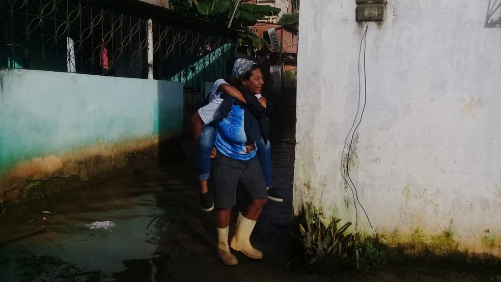 Mulher com filho nas costas para passar por rua alagada em Salvador na manhÃ£ desta quinta-feira (25) â?? Foto: Cid Vaz/TV Bahia
