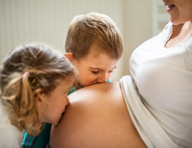 Irmãos beijam a barriga da mãe, grávida de uma terceira criança (Foto: Getty Images)