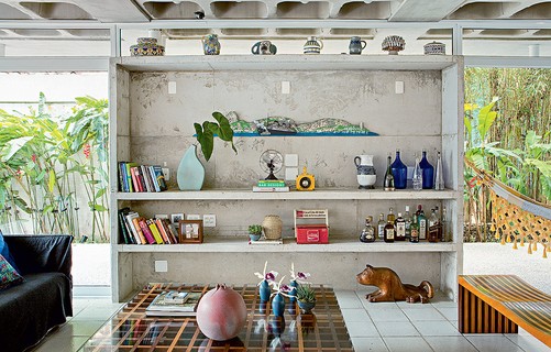 Solta do teto, a estante é uma caixa de concreto. Fechada no alto por caixilho com vidro fixo, tem prateleiras do mesmo material. O projeto é do arquiteto Gustavo Calazans