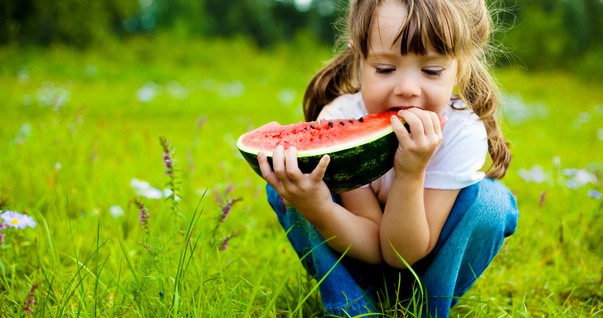 Criança comendo melancia ao ar livre (Foto: Shutterstock)