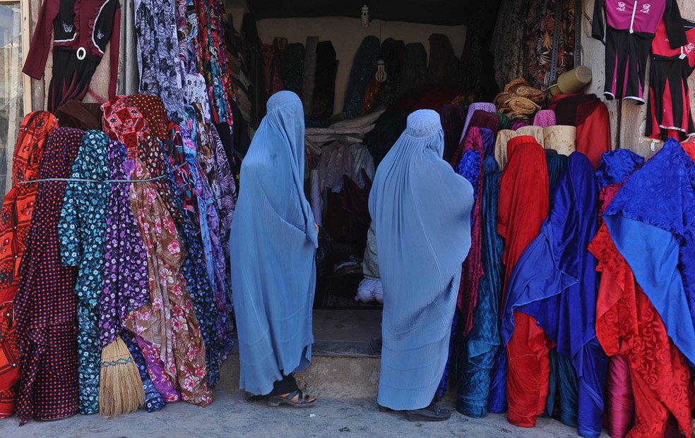 Mulheres afegãs vestidas de burca olham roupas em frente de uma loja de roupas em Herat em 2012. — Foto: Aref Karimi/AFP