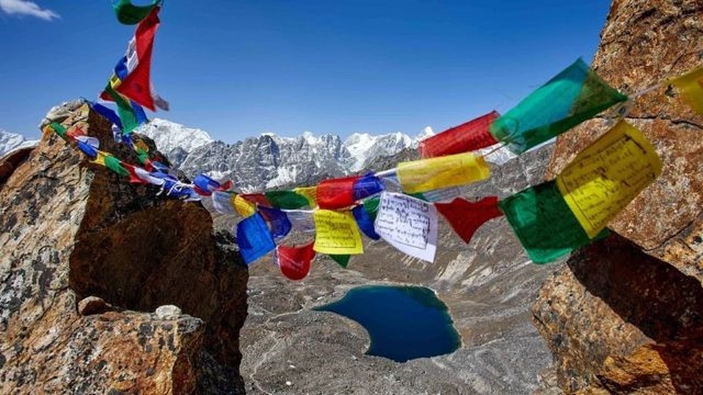 Picos no Himalaia com bandeiras coloridas com escritos tibetanos — Foto: STUART BUTLER