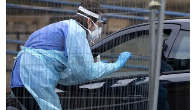 Profissional de saúde usa um cotonete para coleta de amostras pela janela do carro em um 'drive-thru' de exames em Edimburgo (Foto: BBC News)
