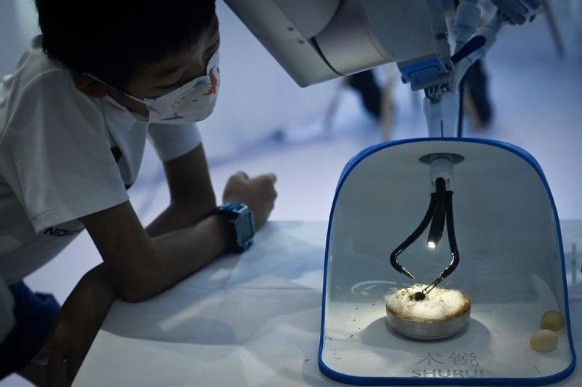 Uma criança observa um braço robótico utilizado em cirurgias descascando cascas de ovos de codorna — Foto: Wang Zhao / AFP