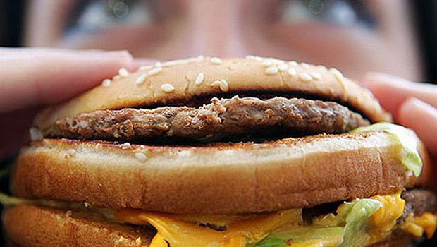 Jovem come hamburguer em lanchonete Fast food Junk food (Foto: Getty Images)