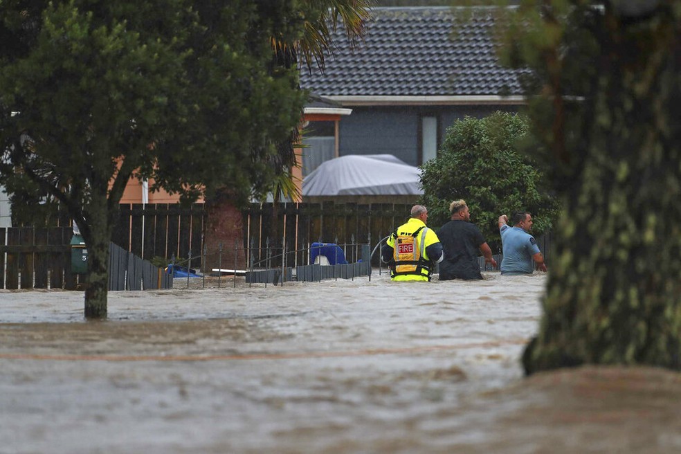 Equipes de emerg&ecirc;ncia e um homem atravessam as &aacute;guas da enchente em Auckland, Nova Zel&acirc;ndia, sexta-feira, 27 de janeiro de 2023. &mdash; Foto: Hayden Woodward/New Zealand Herald via AP