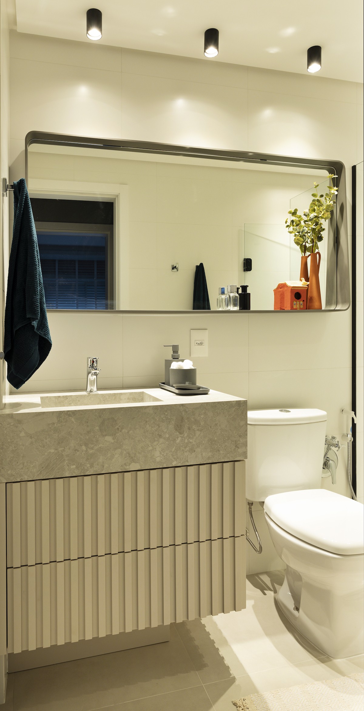BANHEIRO | A ideia do banheiro social foi dar uma "cara"de lavabo. O espelho com moldura orgânica em aço inox vira uma prateleira. A marcenaria tem um ar dinâmico (Foto: Mariana Boro / Divulgação)