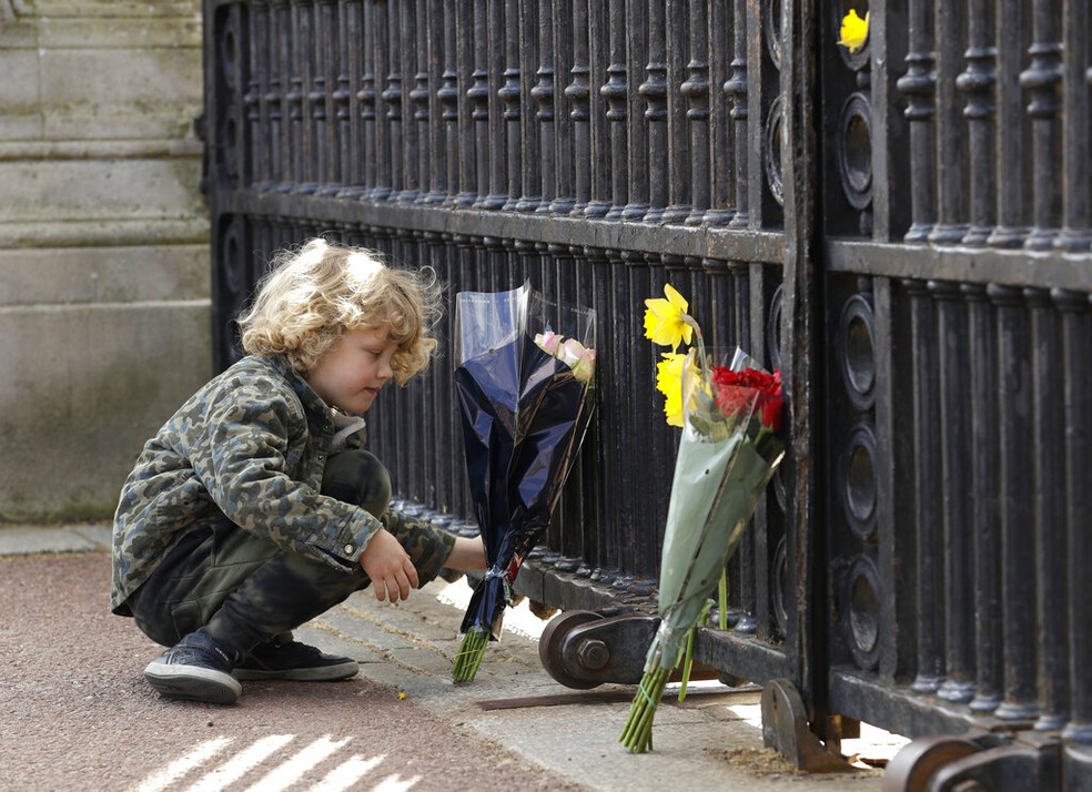 Menino coloca flores em frente ao portão do Palácio de Buckingham, em Londres, após o anúncio da morte do príncipe Philip, marido da rainha Elizabeth II, em 9 de abril de 2021 — Foto: Matt Dunham/AP
