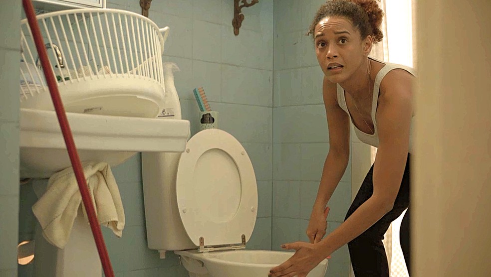 No meio de sua faxina no banheiro, Vitória (Taís Araujo) ouve a campainha — Foto: Globo