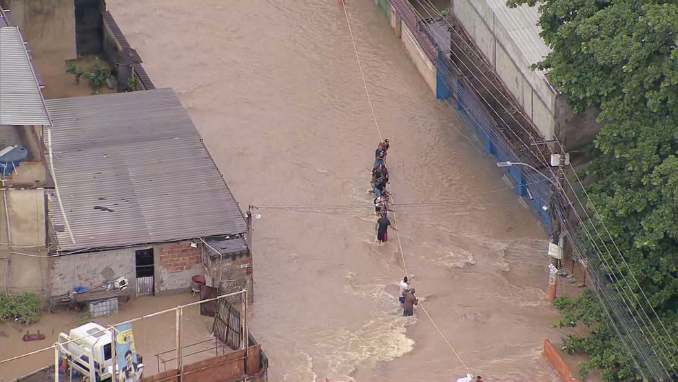 Em Belford Roxo, moradores esticaram uma corda sobre a ponte do Rio Botas, que transbordou — Foto: Reprodução/ TV Globo
