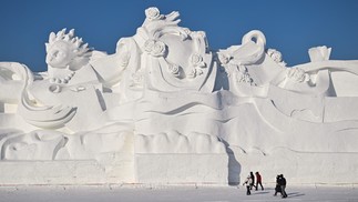 Pessoas caminham ao lado de uma escultura gigante de neve durante megaexposição na província de Heilongjiang, no nordeste da China — Foto: HECTOR RETAMAL/AFP